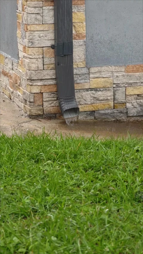Water streaming down gutter pipe onto grassy residential lawn Stock Footage 307494693