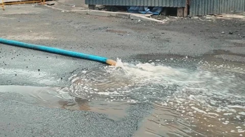 Water streams from a blue pipe and gathers on the ground in an open space. The Stock Footage 339095783