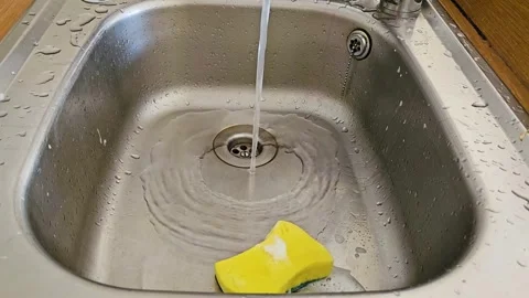 Water Streams Into Clean Kitchen Sink With Yellow Sponge Floating on Surface Stock Footage 301805933