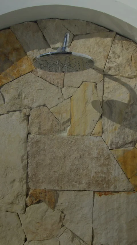 Water streams from a shower head mounted on a natural stone wall Stock Footage 339197730