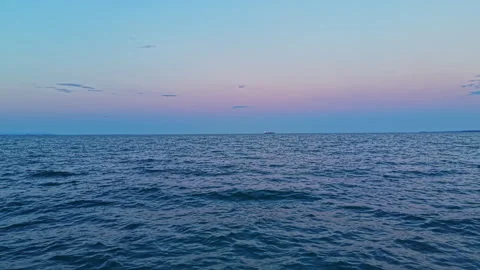 Water surface under pink and blue sky at dusk with distant ship and birds flying Stock Footage 345480657