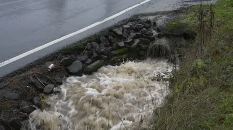 Water surging out of a pipe into a roadside drainage ditch, car passes by Stock Footage 68950732
