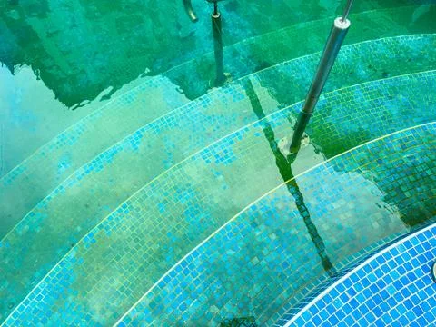 Water surrounds steps in a circular pool with blue tiles during a sunny day Stock Photos
