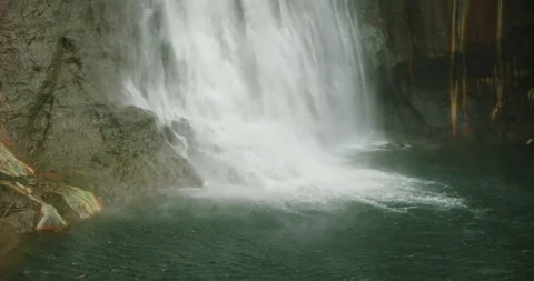 Water from a tall waterfall splashes into a calm pool surrounded by rocky walls Stock Footage 326014676