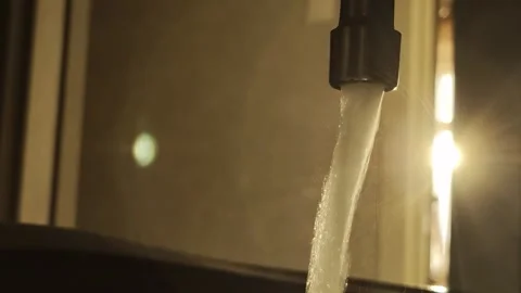 Water from the tap flows against the backdrop of the sunset. Water consumption Stock Footage 317087754