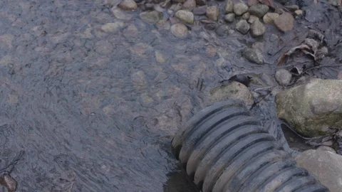 Water trickling/spilling from plastic pipe creating a small creek in slow motion Stock Footage 88683487