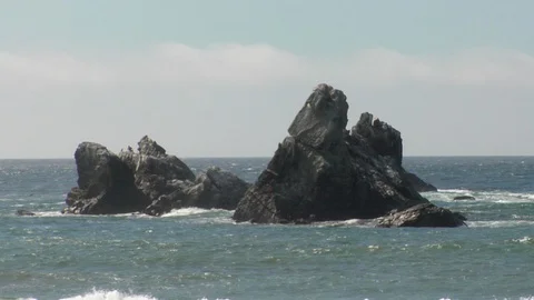 Water waves surround big ocean rocks on island beach Stock Footage 125341387