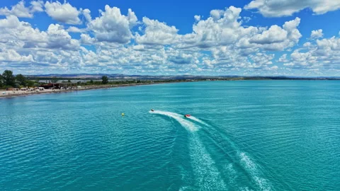 Watercraft navigate clear blue waters near a beach under a cloudy sky during Stock Footage 341398256