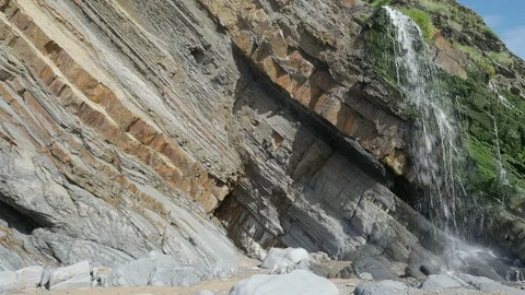 Waterfall and the distinctive colourful strata cliffs at Sandymouth Beach Stock-Footage 86500212