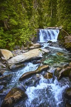 Waterfall and Stream Flowing Through Forest in Lush Mountain Landscape Stock Photos