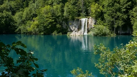 Waterfall from behind tree branches falling in clear blue lake in Plitvice Park Stock Footage 89159731