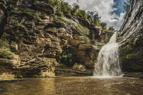 A waterfall with a big fall. It is next to a mountain with a huge hole from w Stock Photos