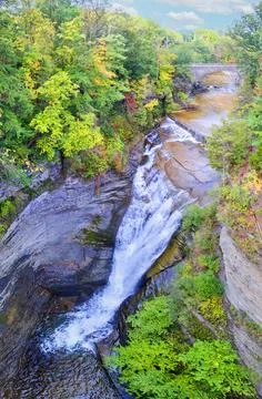 Waterfall into canyon surrounded by fall trees with stone arch bridge in 스톡 사진