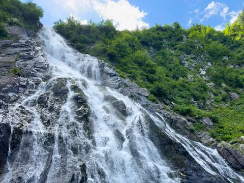 A waterfall cascades down a mountain, surrounded by trees and lush vegetation Stock Photos