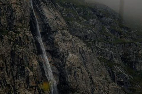 Waterfall cascades down rocky cliffs surrounded by misty mountains. The scene Stock Photos