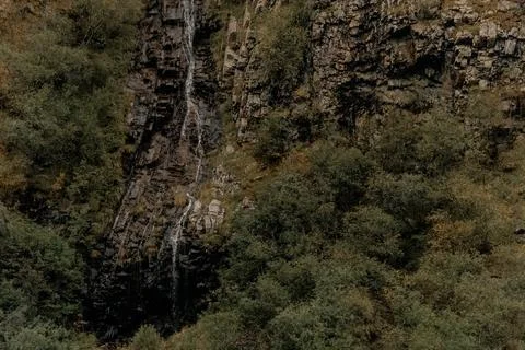 Waterfall cascades down rocky cliffs surrounded by misty mountains. The scene Stock Photos