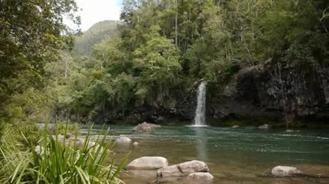 A waterfall cascades into a flowing river Stock Footage 11235915