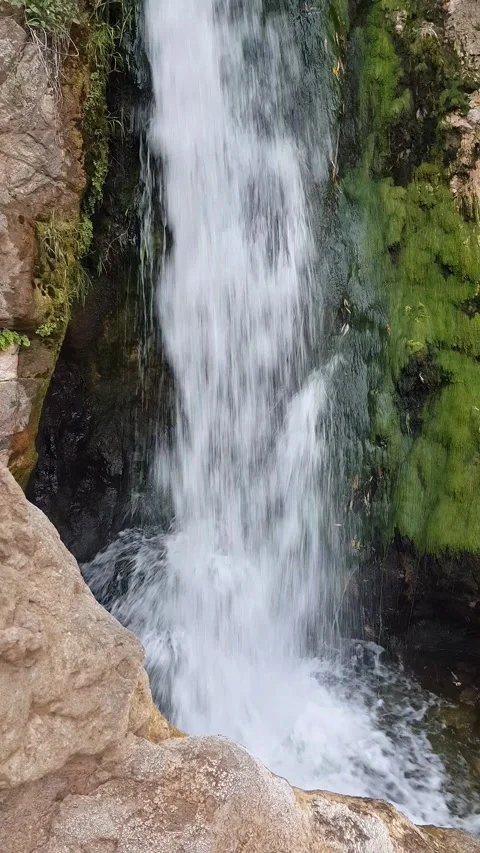 The waterfall cascades gracefully between rugged rocks, showcasing flowing water Stock Footage 314282692