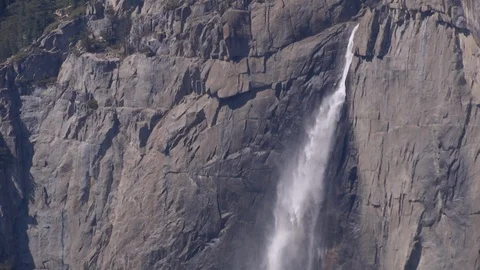 Waterfall cascades over the edge of a steep cliff into the valley Stock Footage 99088119