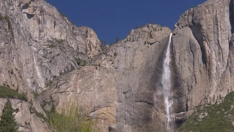 Waterfall cascades over the edge of a steep cliff into the valley Stock Footage 99088347