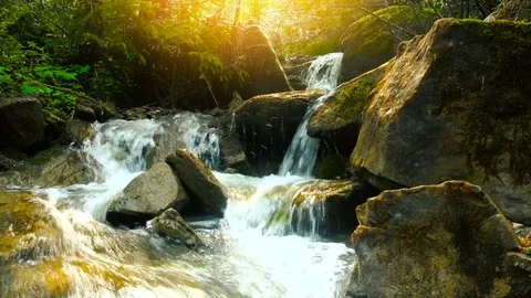 Waterfall cascades in the warm sunset light with mossy stones and rocks along it 스톡 동영상 76792453