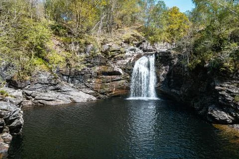 Waterfall cascading into a deep pool amidst lush forest in the Scottish Stock Photos