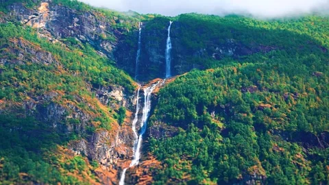 Waterfall cascading down a green mountain beside Norwegian fjord Stock-Footage 341328210