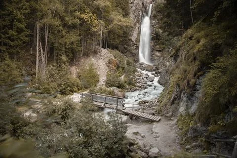 Waterfall cascading down mountain forest with wooden bridge Stock Photos