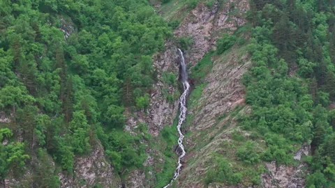 Waterfall cascading down mountainside covered in lush green forest Stock Footage 289656736