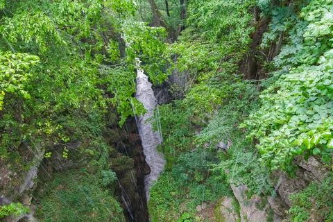 Waterfall cascading down narrow gorge in lush green forest during summer rain Stock Photos