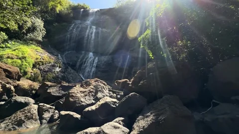 Waterfall Cascading Down Rocky Cliff, Sun Rays and Lens Flare, Wide Shot Stock-Footage 324769934