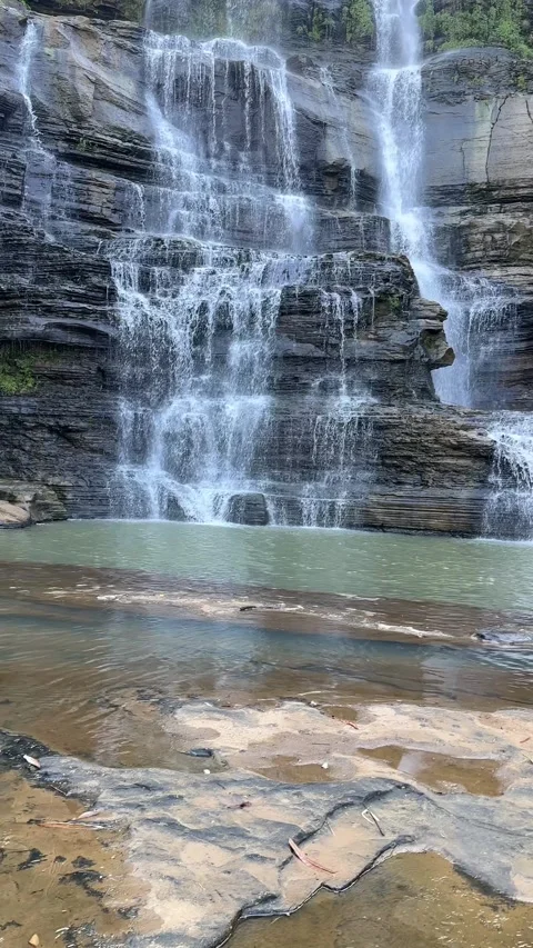 Waterfall Cascading Down Rocky Cliff, Stream in Foreground, Vertical Shot Stock Footage 324772729