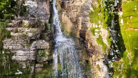 Waterfall cascading down rocky cliff with lush green moss and flowing spring Stock Footage 327730191