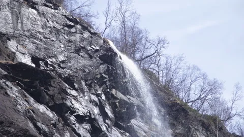 Waterfall Cascading Down Rocky Cliff with Bare Trees in Spring, Kjosfossen Stock Footage 340357654