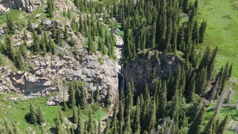 Waterfall cascading down rocky cliffs in green valley Video stock 312435139