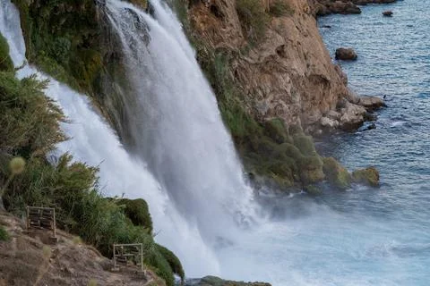 Waterfall Cascading Down Rocky Cliffs Into Turquoise Sea at Sunset Near Coastal Stock Photos