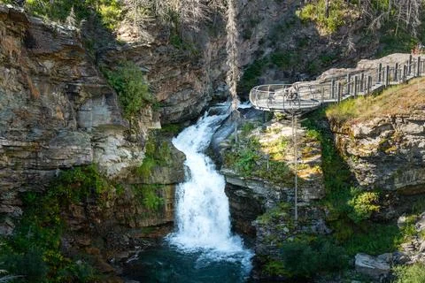 Waterfall cascading down rocky cliffs with wooden bridge in bright sunshine. Stock Photos