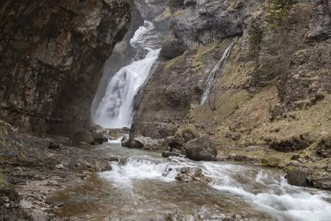 Waterfall cascading down rocky cliffs into a valley river Stock Photos