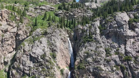Waterfall cascading down rocky mountain slope surrounded by green vegetation Stock Footage 312159797