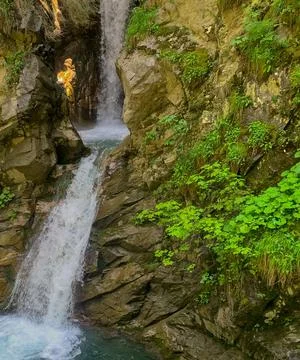 Waterfall cascading down a rocky mountain with patches of grass Stock Photos