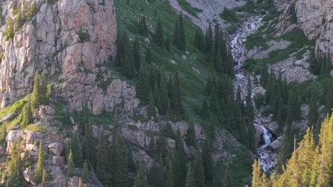 Waterfall cascading down rocky mountainside covered in lush greenery Stock Footage 312447602