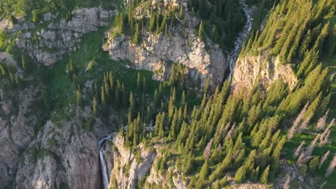 Waterfall cascading down rocky mountainside surrounded by lush green forest Vídeos de archivo 312447737