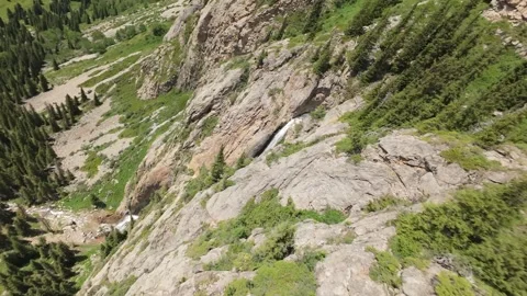 Waterfall cascading down rocky mountainside in lush green valley Stock-Footage 312725535