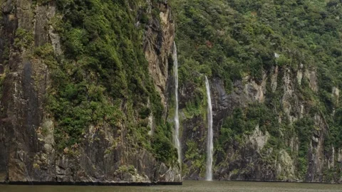Waterfall cascading down steep cliffs into Milford Sound fjord, New Zealand Stock Footage 330950238