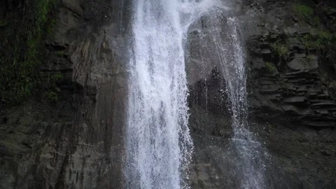 Waterfall cascading down steep rocky cliff surrounded by vegetation Stock Footage 299736824
