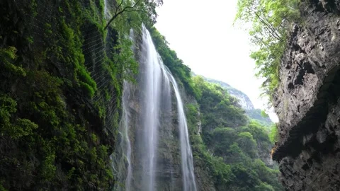 Waterfall cascading down steep rocky cliffs in a lush green mountain forest 스톡 동영상 342215667