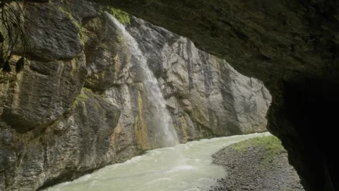 Waterfall cascading into gorge river from cave view in Swiss Alps Video stock 320103466