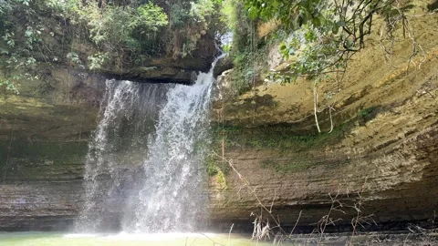 Waterfall Cascading into Green Pool, Lush Jungle Cliff, Panning Shot Stock Footage 325645944