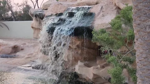 A waterfall cascading over rocks into a pool with a crocodile in the background 스톡 동영상 318833133
