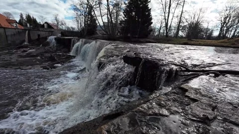 Waterfall cascading over rocky ledge beside a historic mill, static shot Stock Footage 337555309